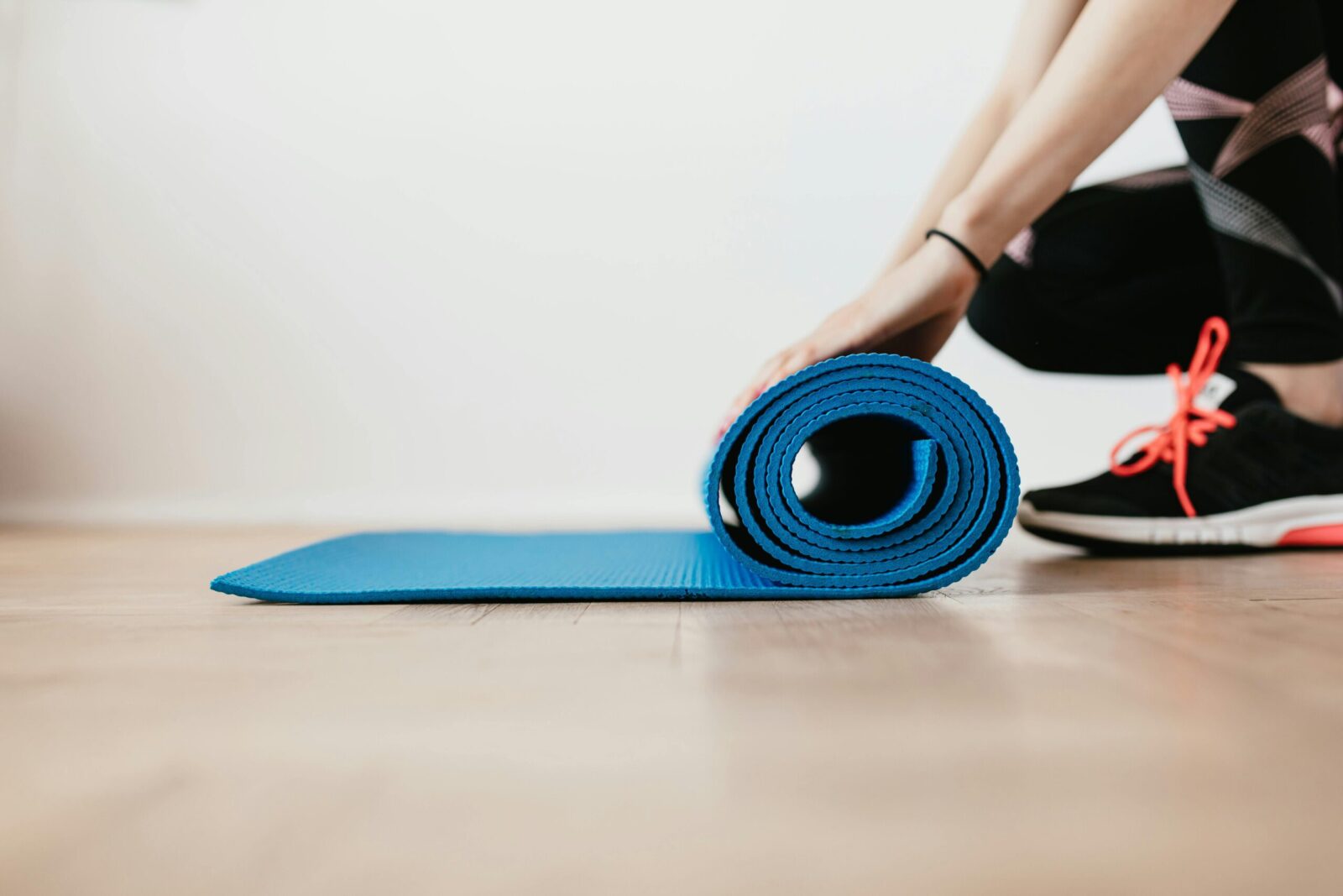 Close-up of a woman preparing for an indoor workout by rolling a blue yoga mat.